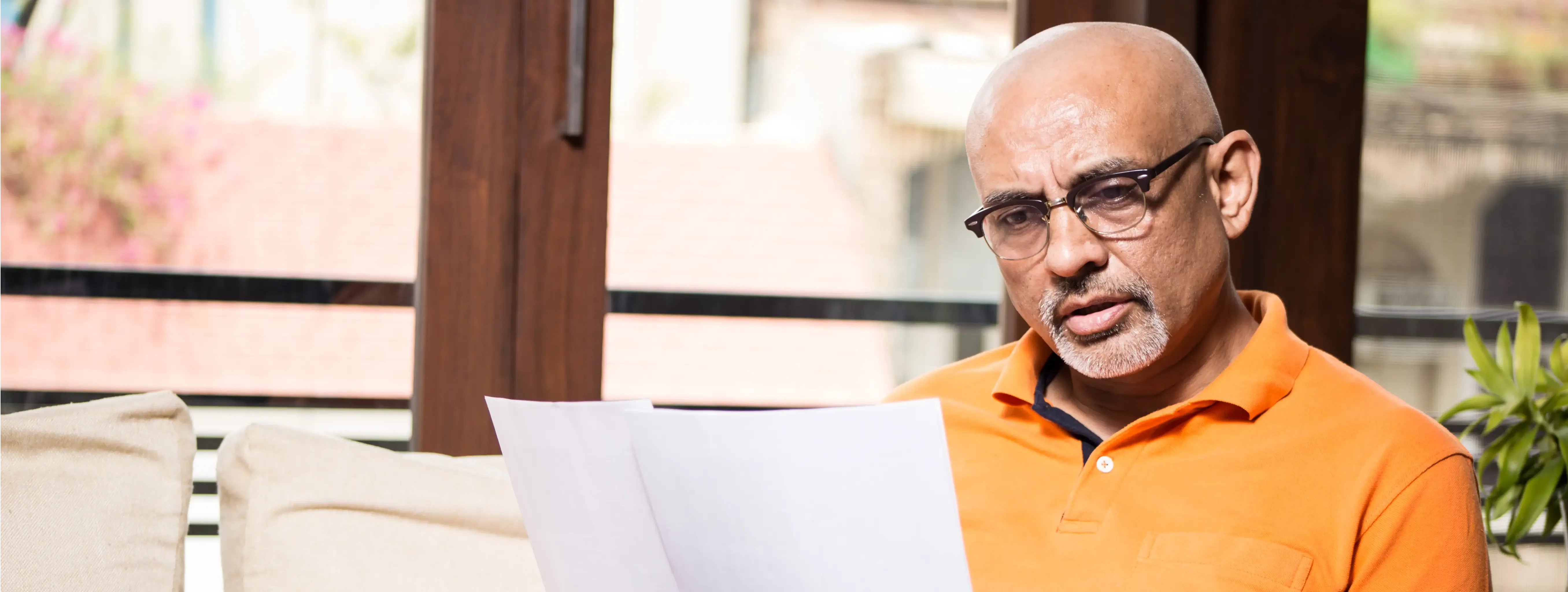 older male sitting looking at papers laptop on legs